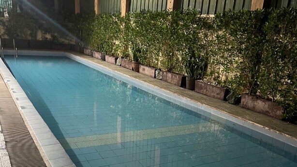 A swimming pool with tiled edges, surrounded by a low brick wall and potted plants. - Spacious family-friendly apartment with Balcony! (Muntinlupa)