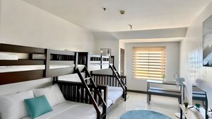 A modern hotel room with a bunk bed, a sofa, a desk, and a large window with blinds. - Spacious family-friendly apartment with Balcony! (Muntinlupa)
