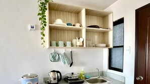 A compact kitchen with a microwave, stove, and sink. There are cabinets above the counter and a small refrigerator to the left. - Spacious family-friendly apartment with Balcony! (Muntinlupa)