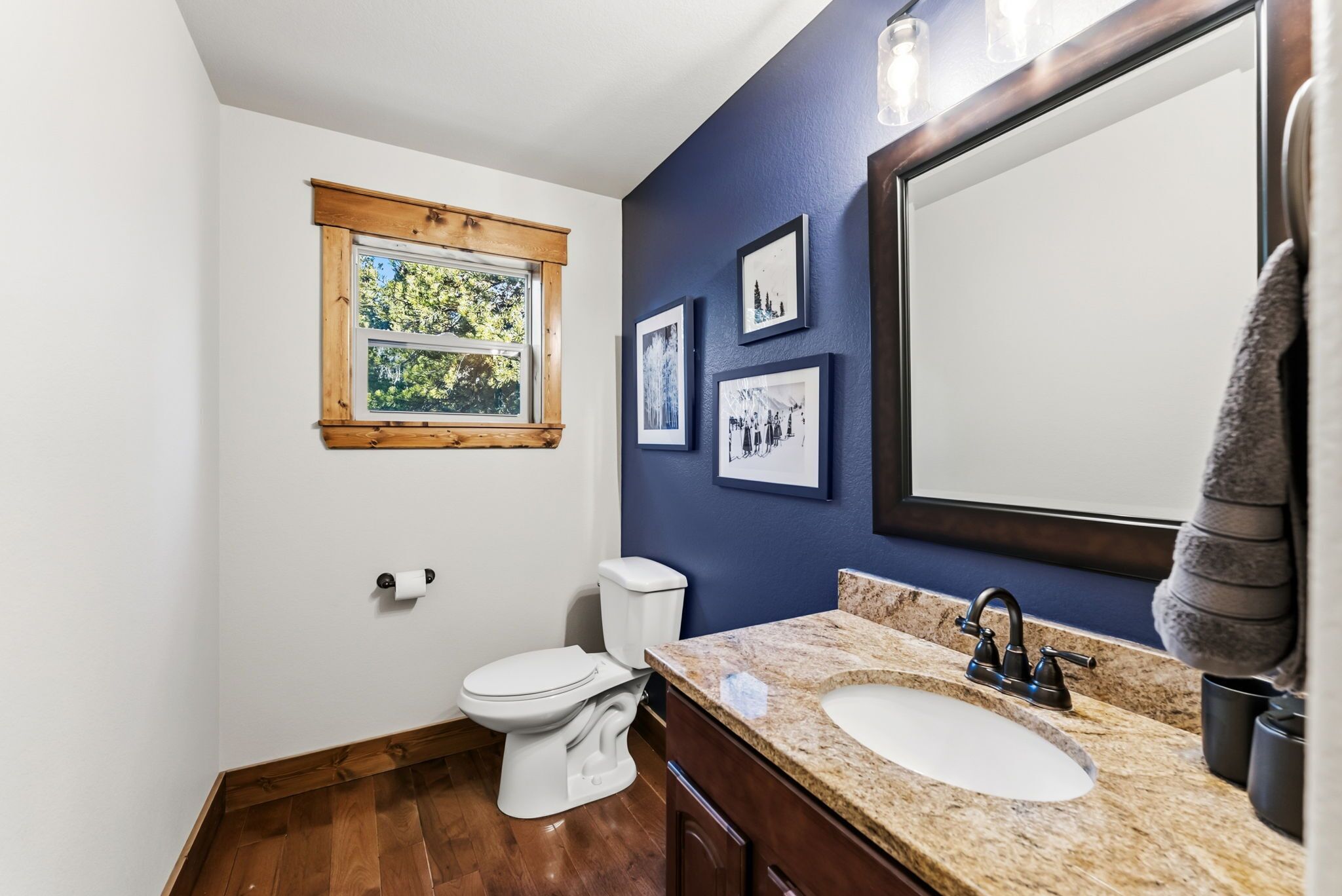 Ein Badezimmer mit einer weißen Toilette, einem Waschbecken mit Marmorplatte, einem großen Spiegel und gerahmten Bildern an der Wand.
