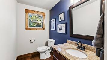 Ein Badezimmer mit einer weißen Toilette, einem Waschbecken mit Marmorplatte, einem großen Spiegel und gerahmten Bildern an der Wand.
