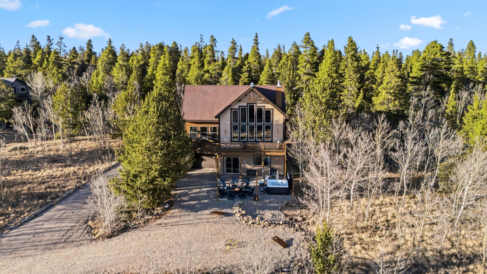 A two-story lodge with a large deck, surrounded by dense forest.
