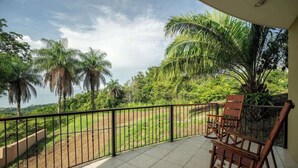 A balcony with a view of a lush landscape, including palm trees and a distant body of water. - Amazing Mountain & Ocean Views (Playa Hermosa)