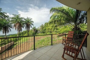Ein Balkon mit Blick auf eine üppige Landschaft, darunter Palmen und ein weiter Wasserblick.