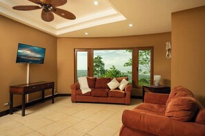 Ein Wohnzimmer mit Sofa, Fernseher, Deckenventilator und großen Fenstern.
