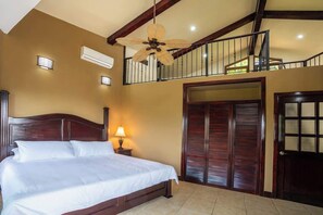 Ein Schlafzimmer mit Bett, Deckenventilator, Klimaanlage, Nachttisch, Lampe, Kleiderschrank und einem Balkon.