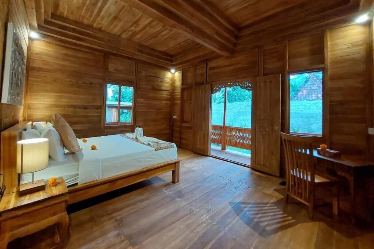 Een houten kamer met een bed, nachtkastje en een bureau met stoelen.
