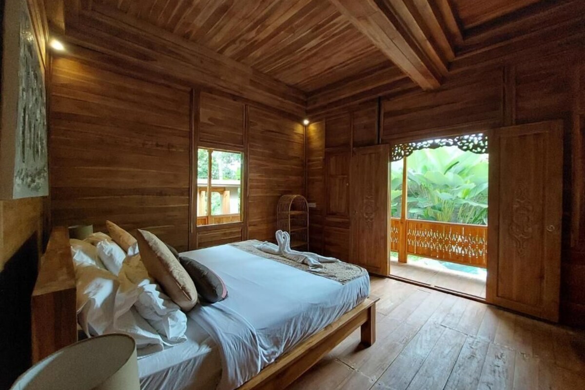 Een houten kamer met een bed, een raam en een deur naar buiten.