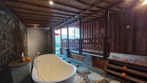 Une salle de bain avec une baignoire sur pieds, des murs en pierre et un plafond en bois.