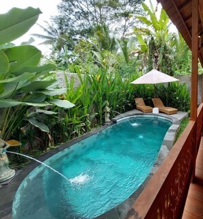 A rectangular pool with clear blue water, surrounded by lush greenery and a wooden deck. - D'Ethnic Ubud Joglo View Villas by EPS (Ubud)