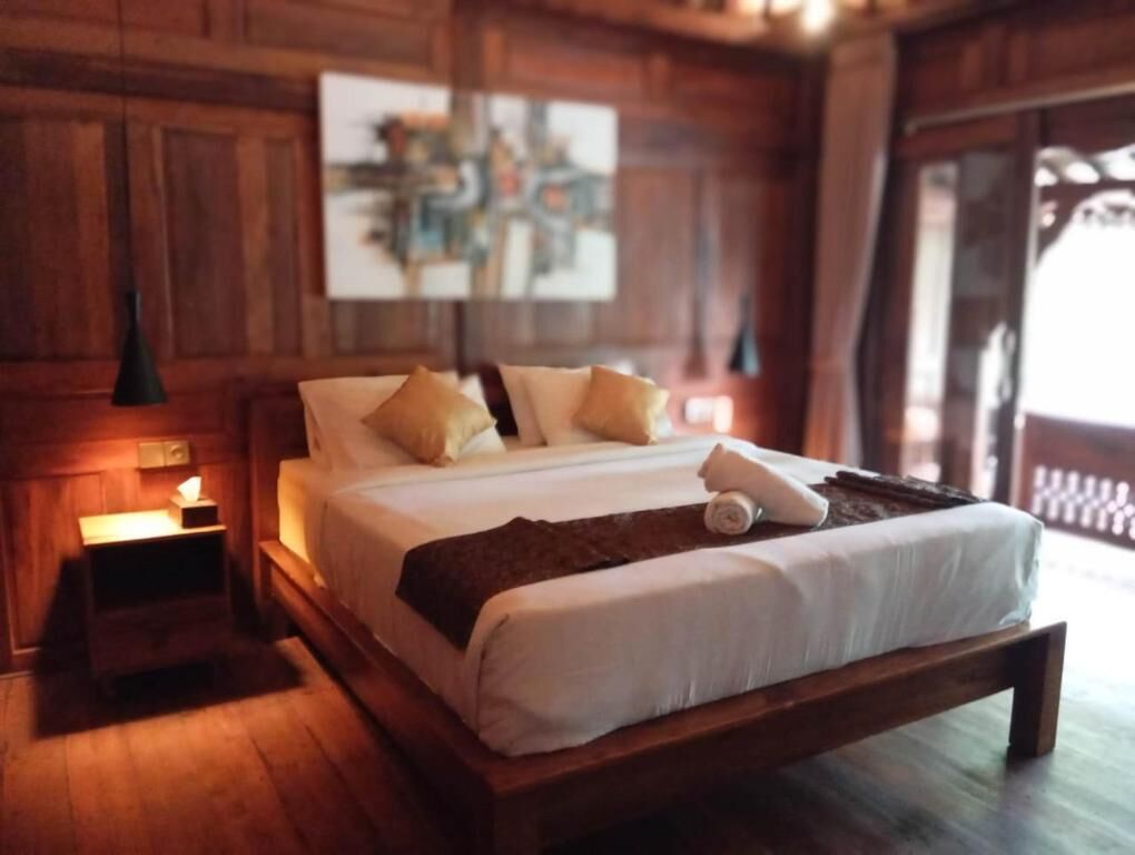 A wooden-framed bed with white linens, a bedside lamp, and a painting on the wall.