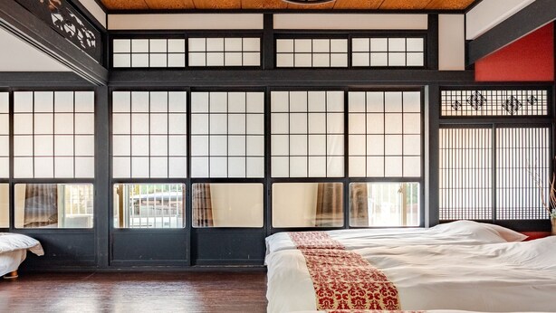 Una habitación tradicional japonesa con suelo de tatami, puertas shoji y una cama con colcha de diseño rojo y blanco.