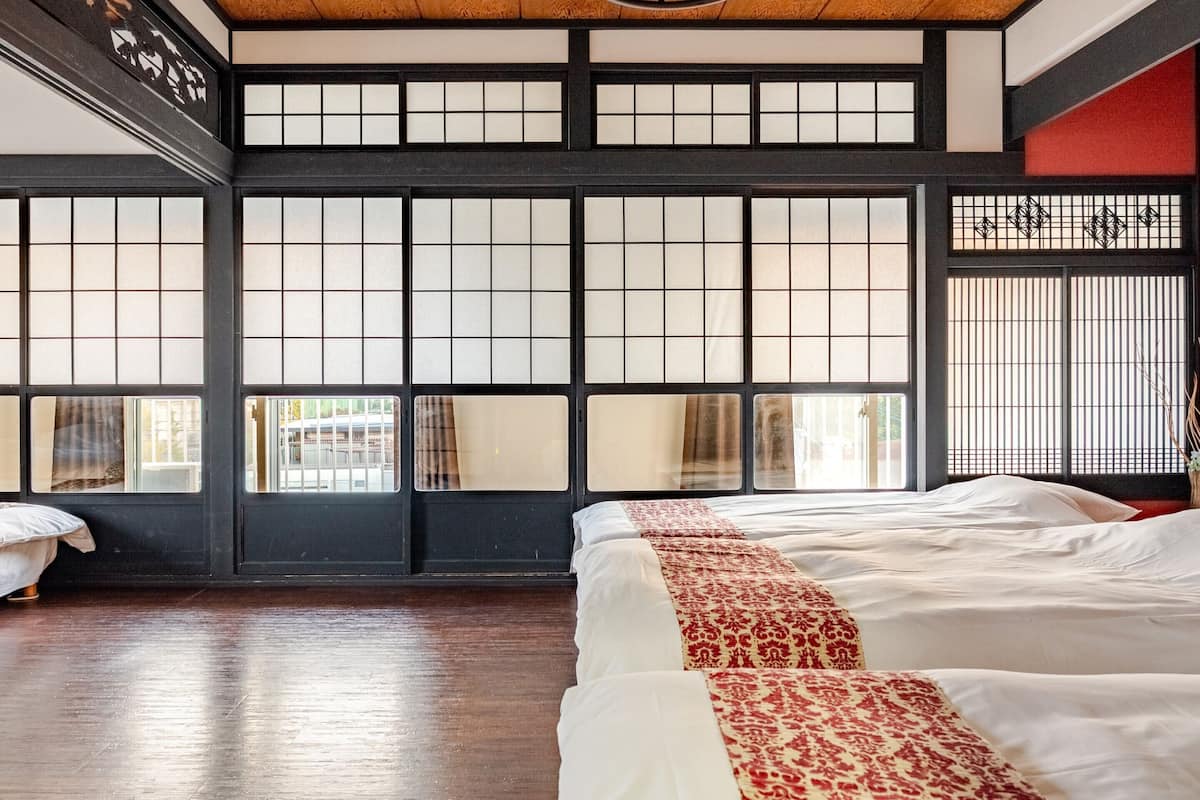 Una habitación tradicional japonesa con suelo de tatami, puertas shoji y una cama con colcha de diseño rojo y blanco.