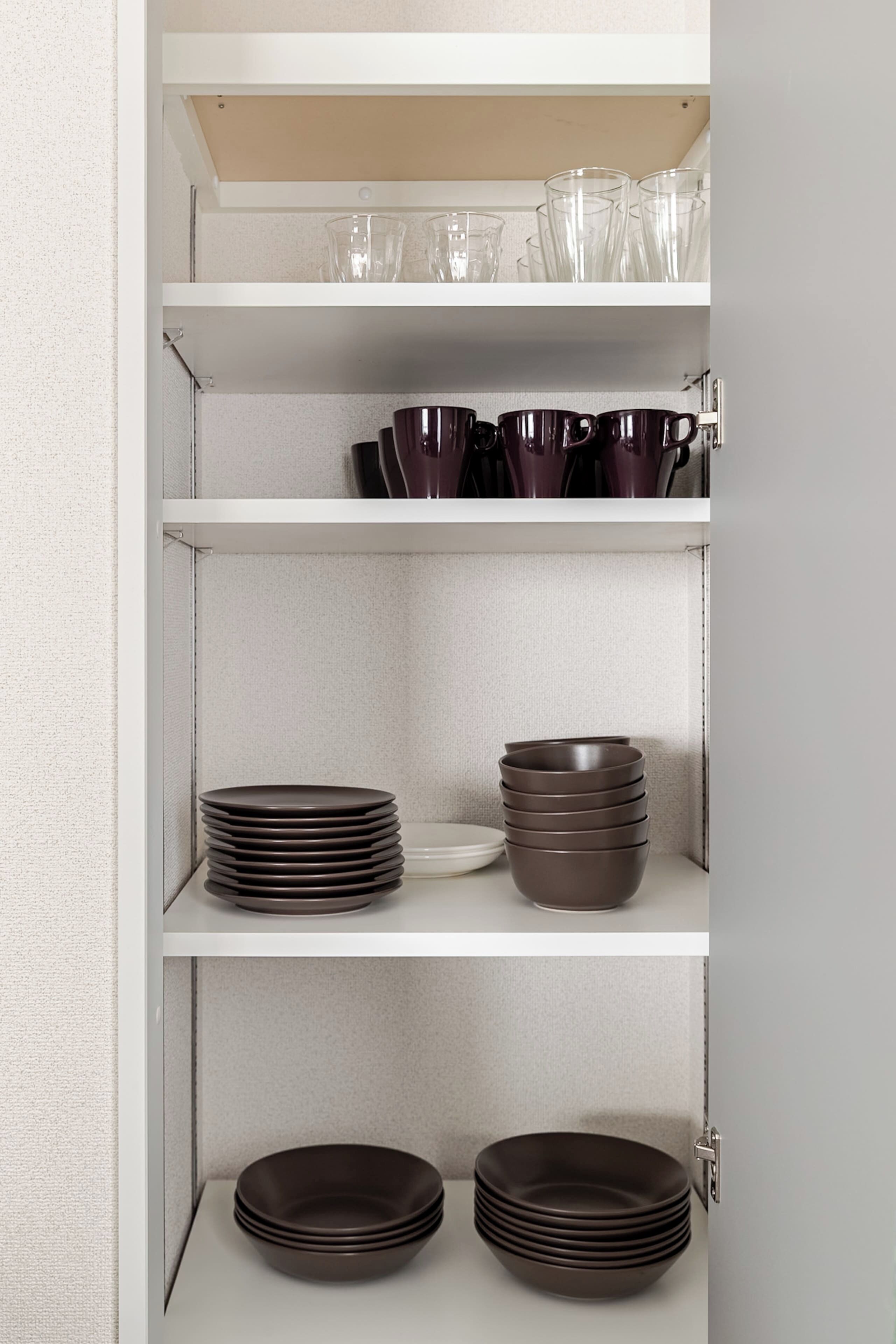 Ein Küchenschrank mit Regalen, auf denen Teller, Schüsseln und Gläser stehen.
