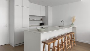 Une cuisine moderne avec des meubles blancs, un îlot central doté de tabourets et un design minimaliste.