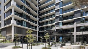 Un bâtiment moderne à plusieurs étages, doté d’une façade en verre, d’un espace extérieur aménagé pour s’asseoir et d’une allée couverte.