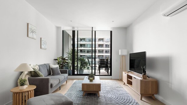 Un salon moderne avec un canapé, une table basse et un meuble pour la télévision. Une grande fenêtre offre une vue sur les bâtiments environnants.