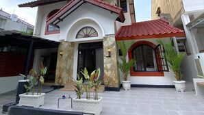 A two-story building with a stone facade, a red-tiled roof, and a covered patio area with potted plants. - Homestay Syariah Merapi View Simply Homy (Ngaglik)