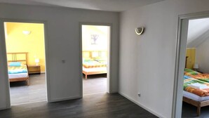 Een ruime kamer met een houten vloer en witte wanden, met een bed met een kleurrijk dekbed en een nachtkastje met een lamp.