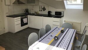 Een moderne keuken met witte kasten, een zwart aanrecht en een eethoek met een tafel voor vier personen.