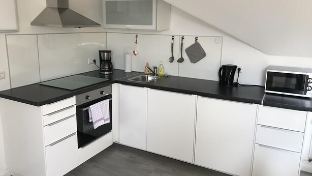 Een moderne keuken met witte kasten, een zwart aanrecht, een fornuis, een magnetron en een hangende pannenrek.