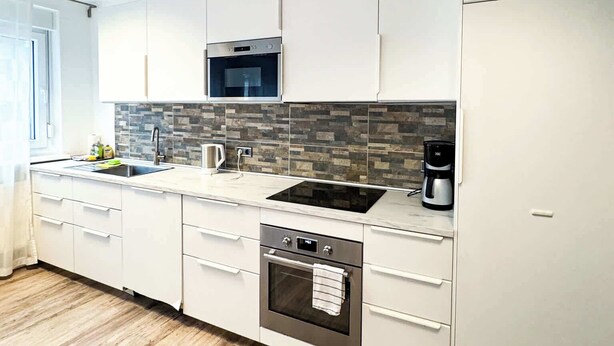 Una cocina moderna con armarios blancos, horno integrado, microondas y cafetera.
