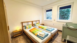 Una habitación con dos camas de madera, un escritorio pequeño, un radiador y ventanas con vistas a árboles.