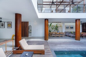 Um interior moderno com piscina, colunas de madeira, área de jantar e obras de arte.
