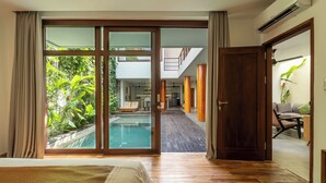 Ein Schlafzimmer mit einer großen SchiebeglasTür, die zu einem Poolbereich führt, Holzboden und Blick ins Freie.