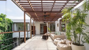 Ein geräumiger Balkon mit einer Pergola, eine Sitzecke mit einer Couch und einem Sitzsack, sowie ein großer Topfpflanze.