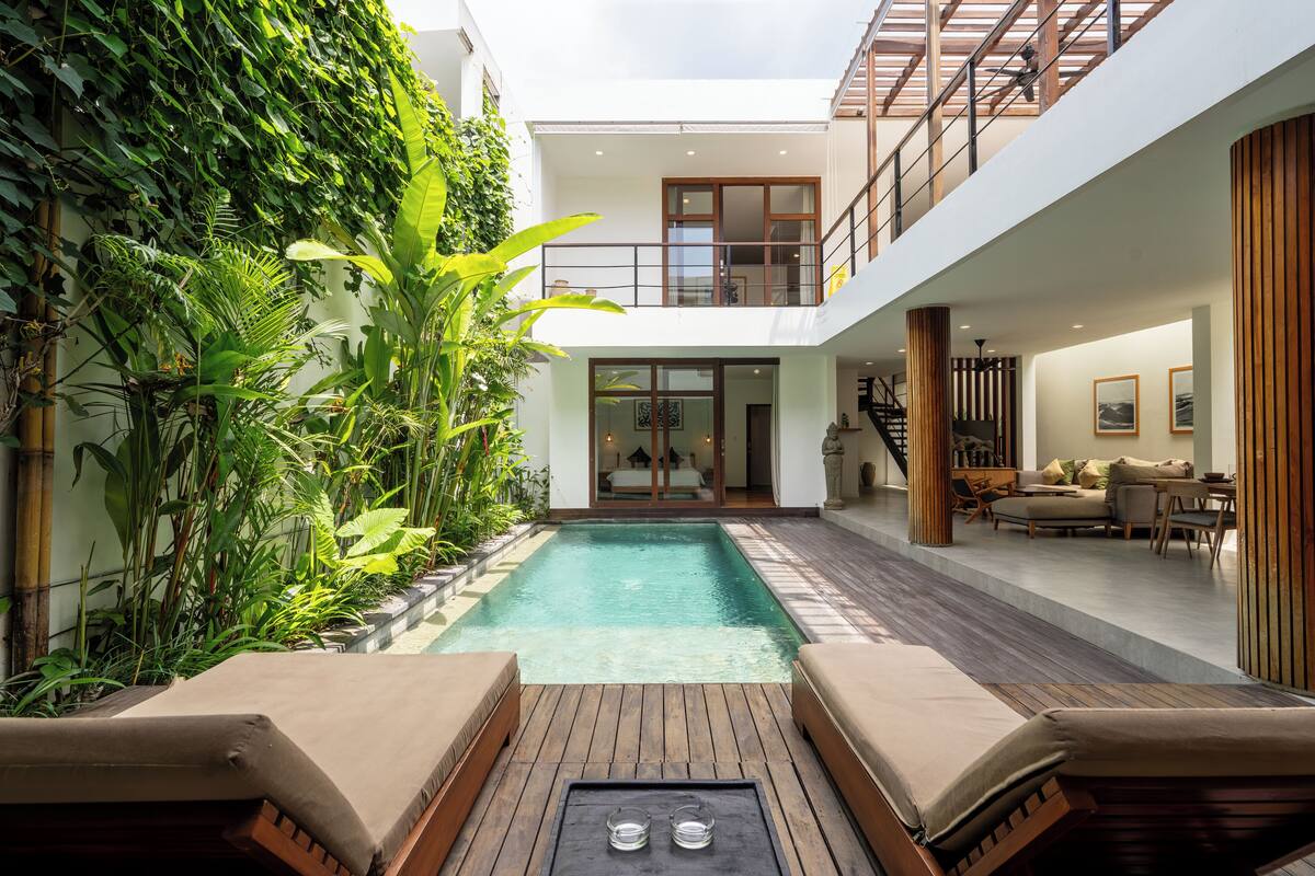 Uma casa moderna com piscina central, deck de madeira e varanda com vista para a piscina.