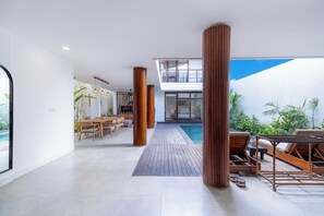 Um interior moderno com área de jantar, colunas de madeira, piscina e vista para o exterior.