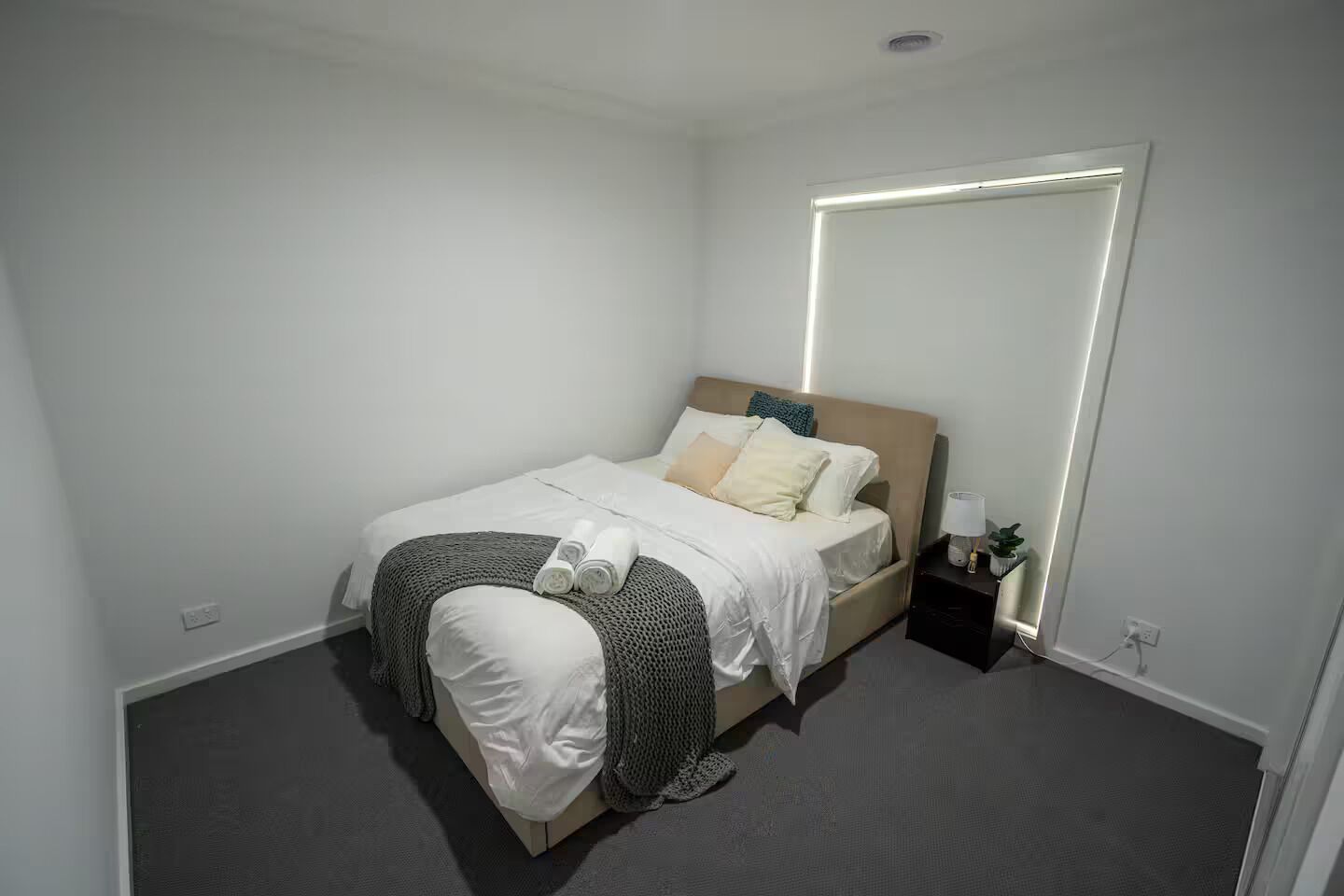A neatly arranged bedroom with a bed, a bedside table with a lamp, and a large mirror on the wall.