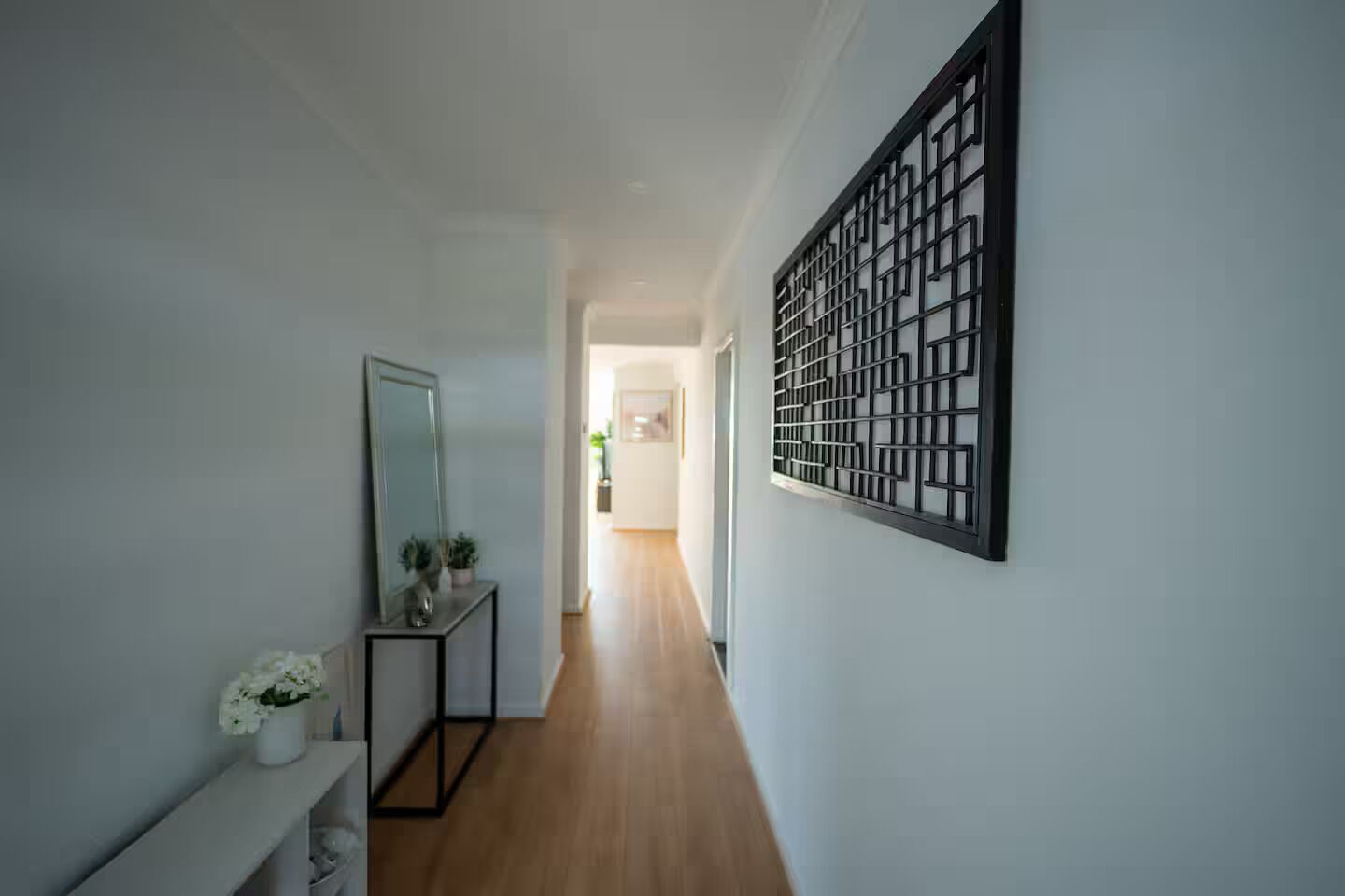 A hallway with a mirror, a console table with a vase of flowers, and a decorative panel on the wall.