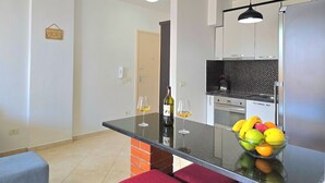Cozinha moderna com ilha central, área de jantar com um banco vermelho e ilha da cozinha com uma tigela de frutas e dois copos de vinho.