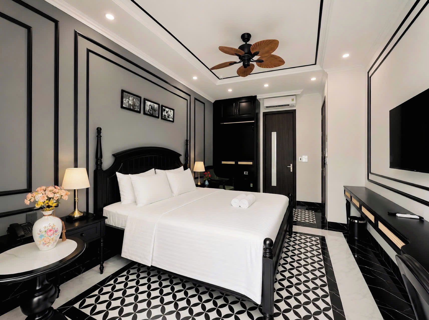 Une chambre d’hôtel avec un lit, des tables de chevet, un téléviseur, un ventilateur de plafond et un sol à motifs.