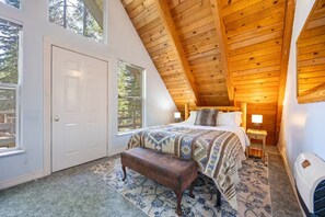 Une chambre avec un plafond en pente, un lit avec une literie à motifs, un banc et une table de chevet avec une lampe.