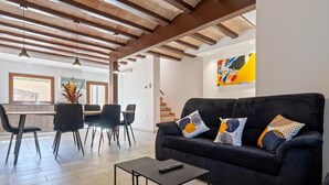 A modern living room with a dark sofa, a coffee table, and a dining area with chairs and a table.