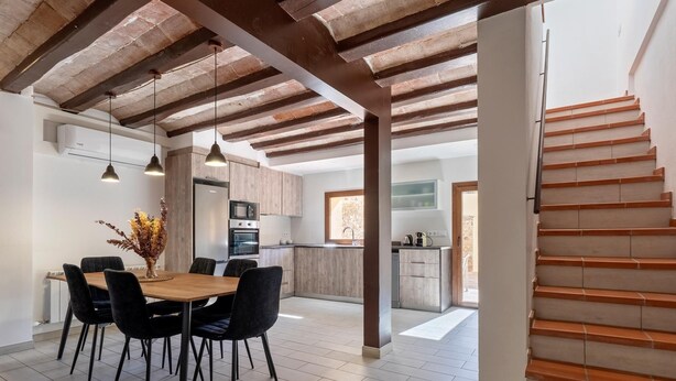A modern kitchen with wooden cabinets, a dining area with a wooden table and chairs, and a staircase with wooden steps.