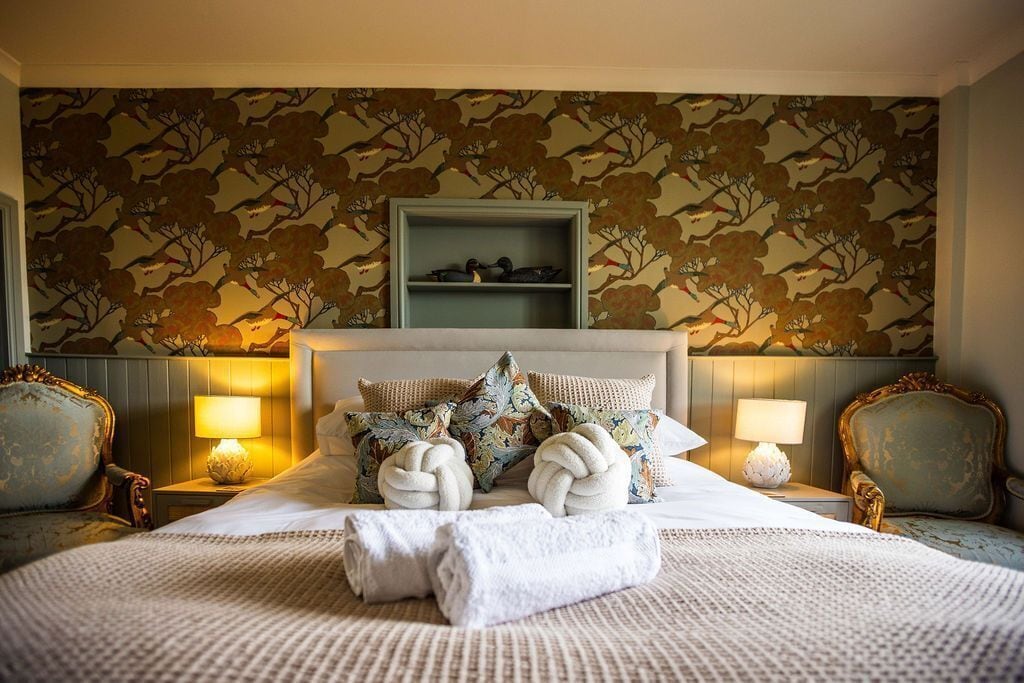 Habitación de hotel con cama, dos mesitas de noche, cabecero y pared con estampado floral.