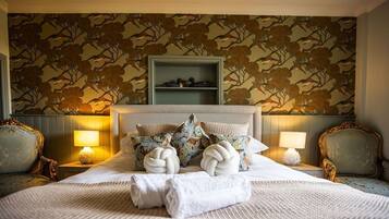 Habitación de hotel con cama, dos mesitas de noche, cabecero y pared con estampado floral.