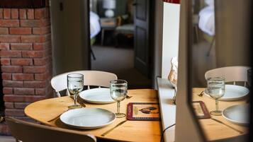 Una mesa de comedor servida con platos, vasos y cubiertos, con una pared de ladrillo y una puerta que da a otra habitación.