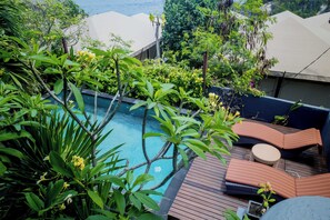 Una piscina rodeada de exuberante vegetación, una terraza de madera y mobiliario exterior.