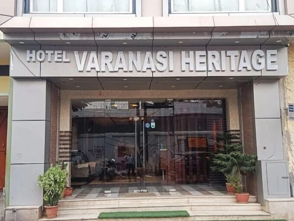 The entrance of Hotel Varanasi Heritage with a clear sign above the door, a glass facade, and potted plants on either side. - Hotel Varanasi Heritage (Varanasi)