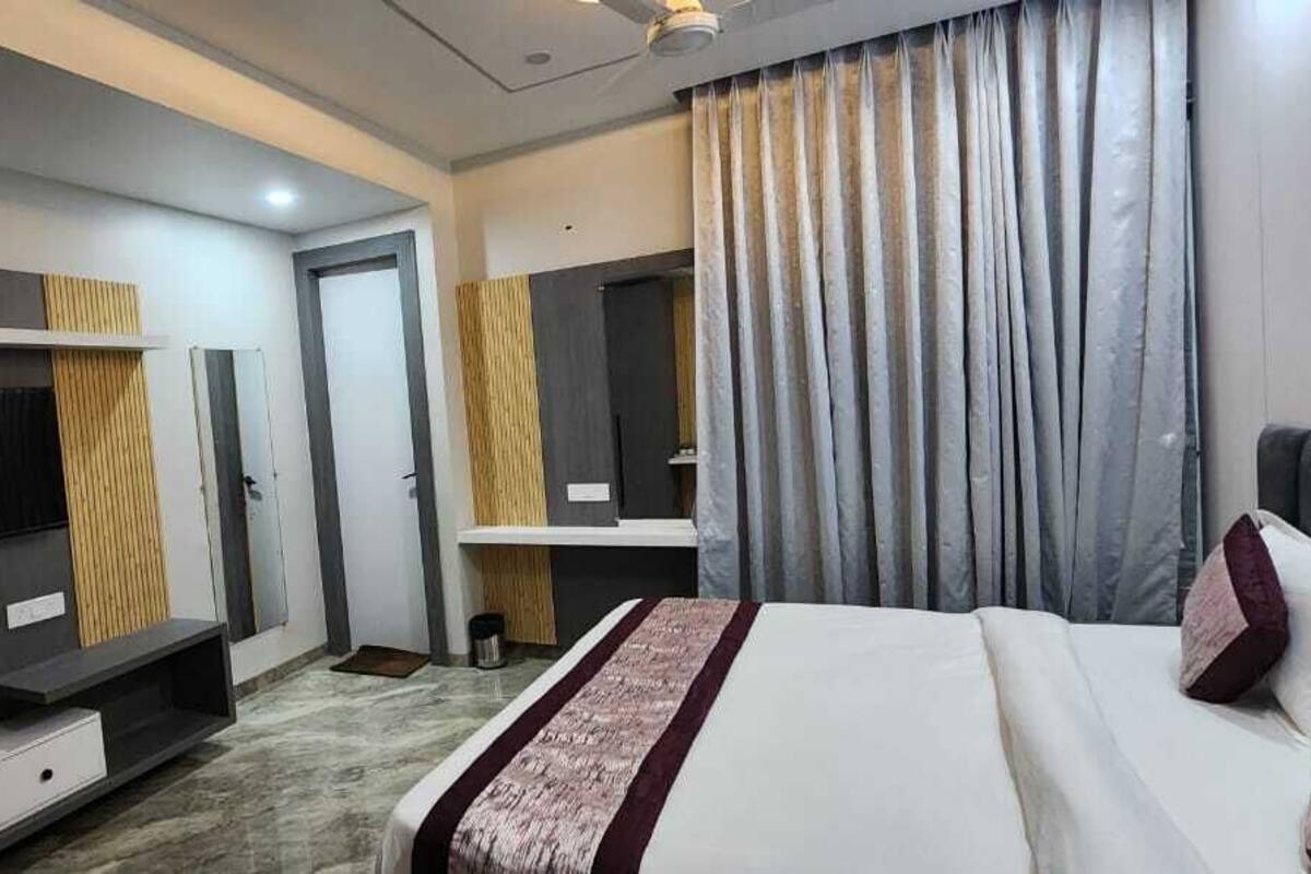 Quarto de hotel moderno com uma cama grande, uma TV de tela plana, um espelho de toucador e uma janela ampla com cortinas.