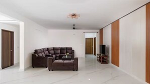 A modern living room with a sectional sofa, a coffee table, and a television on a stand. - Casa Miro by Red Olive 4bhk Hebbal Bangalore (Bengaluru)