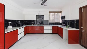 A modern kitchen with a central island, white cabinets, red accents, and a ceiling fan. - Casa Miro by Red Olive 4bhk Hebbal Bangalore (Bengaluru)