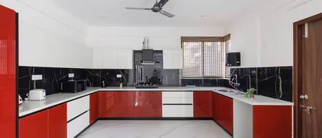 A modern kitchen with a central island, white cabinets, red accents, and a ceiling fan.
