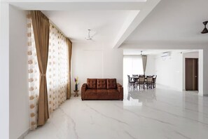 A spacious living room with a brown sofa, a dining area with a table and chairs, and a ceiling fan. - Casa Miro by Red Olive 4bhk Hebbal Bangalore (Bengaluru)
