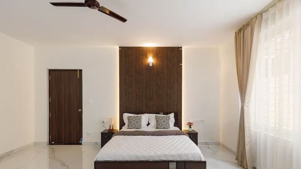 Un dormitorio con una cama, una mesita de noche, un ventilador de techo, un panel de pared de madera y una puerta.